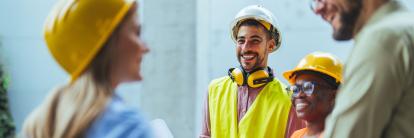 Lächelndes Baustellen‑Team mit Schutzhelmen im Gespräch