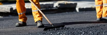 Straßenbauarbeiten: Bauarbeiter in orangefarbener Schutzkleidung verteilen frischen Asphalt auf einer Straße