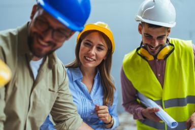 Bauteam mit Schutzhelmen bespricht gemeinsam einen Bauplan