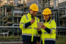 Zwei Mitarbeitende in Schutzkleidung prüfen Daten vor Industrieanlage.