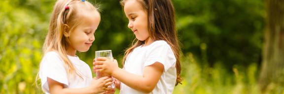 Zei Mädchen halten ein Glas Wasser in der Hand.