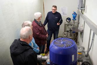 Führung durch technischen Anlagenraum: Mitarbeiter erklärt einer kleinen Gruppe älterer Menschen die Funktionsweise der Wasser- bzw. Pumpentechnik.